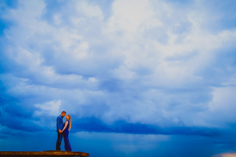 Pareja abrazada bajo un cielo azul dramático, fotografía de amor por Raúl Galavíz